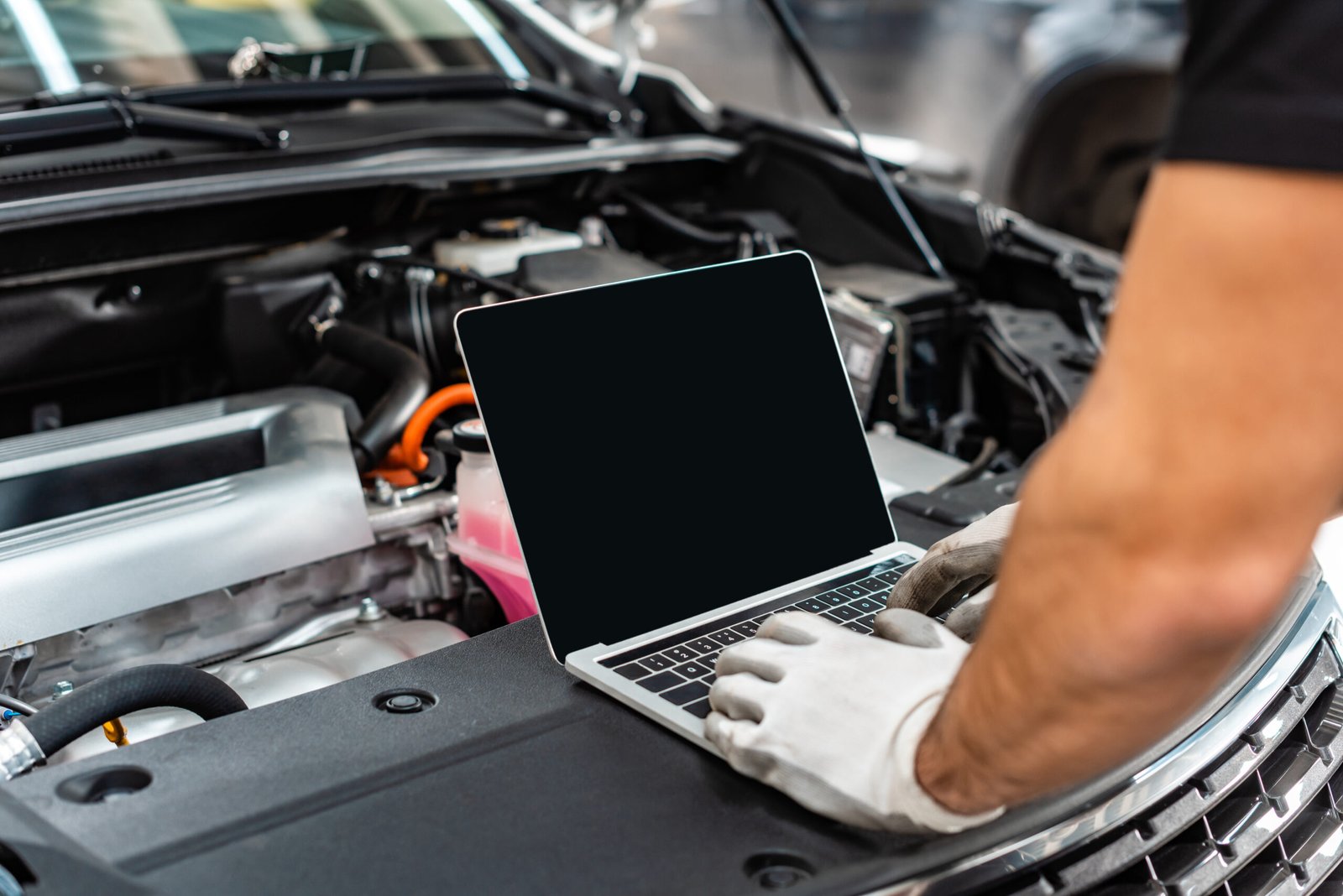 cropped view of mechanic using laptop near car engine compartment